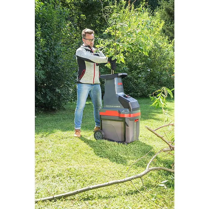 AL-KO Easy Crush Elektro-Walzenhäcksler LH 2810 - Max. Aststärke: 4,2 cm, 2.800 W - Ein Mann benutzt einen AL-KO EASY CRUSH LH 2810 Gartenhäcksler, um Äste zu zerkleinern, mit Bäumen und Gras im Hintergrund.
