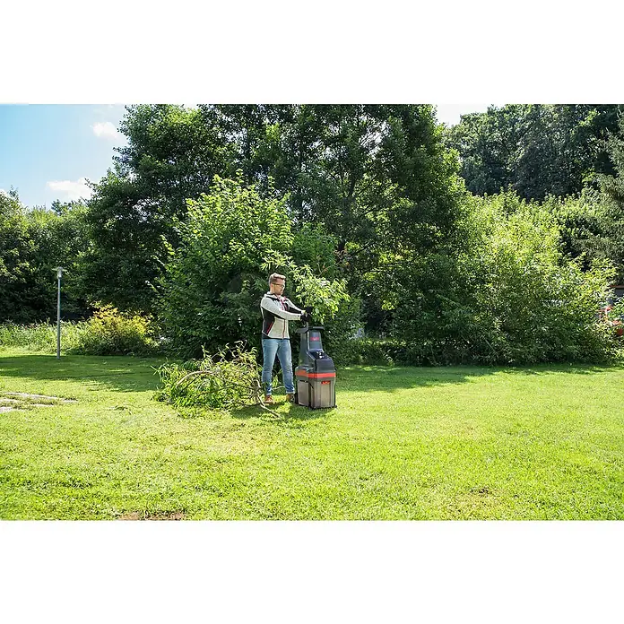 AL-KO Easy Crush Elektro-Walzenhäcksler LH 2810 - Max. Aststärke: 4,2 cm, 2.800 W - Ein Mann benutzt einen Gartenschredder im Freien, um Äste zu zerkleinern. Der Schredder ist rot und grau.