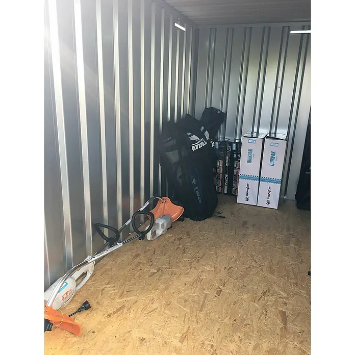 BOS Best of Steel Schnellbaucontainer SC3000+1X2-SE1 x 2,1 x 2,1 m, Stahl, Einzeltür - Aufnahme eines Lagers mit einer STIHL Motorsense, Atoll Rucksäcken und Sevylor Quikpak Kajaks, die ordentlich aufbewahrt werden.