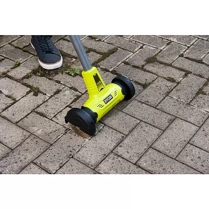 Ryobi ONE+ Limpiador de juntas de batería RY18PCA-0 - 18 V, Iones de litio, Sin batería - Cepillo Ryobi amarillo con cabezal metálico, limpiando malas hierbas de un patio pavimentado.