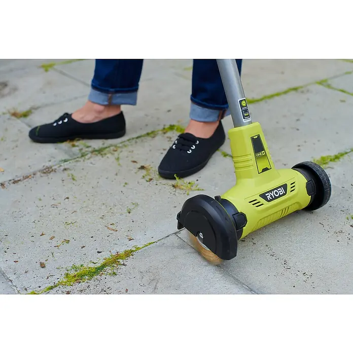 Ryobi ONE+ Limpiador de juntas de batería RY18PCA-0 - 18 V, Iones de litio, Sin batería - Primer plano de un cepillo para juntas Ryobi ONE+ que se utiliza en una superficie pavimentada, con una persona al fondo.