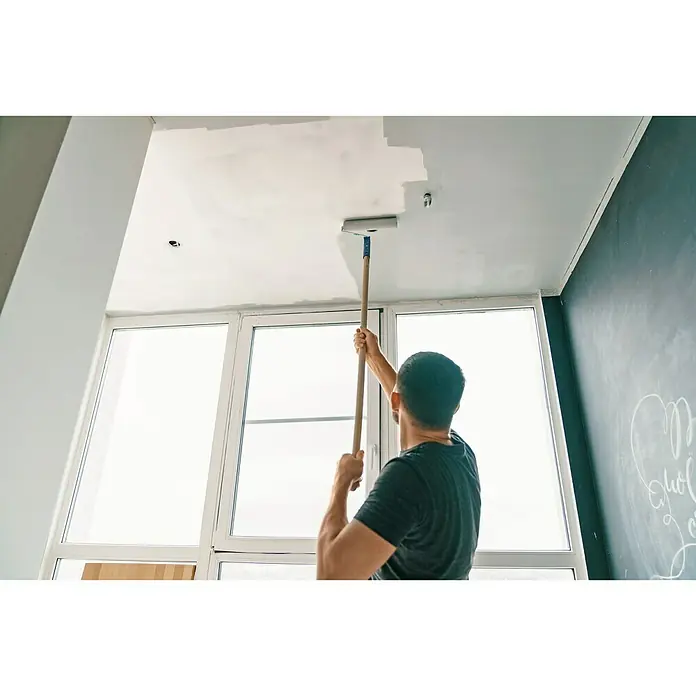 swingcolor Isolierfarbe Universal - 10 l, Weiß - Ein Mann streicht mit einer Farbwalze die Decke eines Raumes, der sich im Renovierungsprozess befindet und hell wirkt.