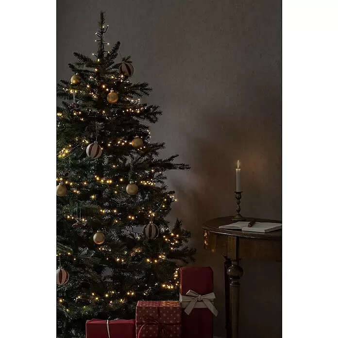 Konstsmide LED-Lichterkette - Innen, Lichtfarbe: Bernstein, Anzahl Leuchtmittel: 400 Stk., Netzbetrieben - Ein festlicher Weihnachtsbaum mit warmen Lichtern und Kugeln, neben Geschenken und einem kerzenbeleuchteten Tisch.