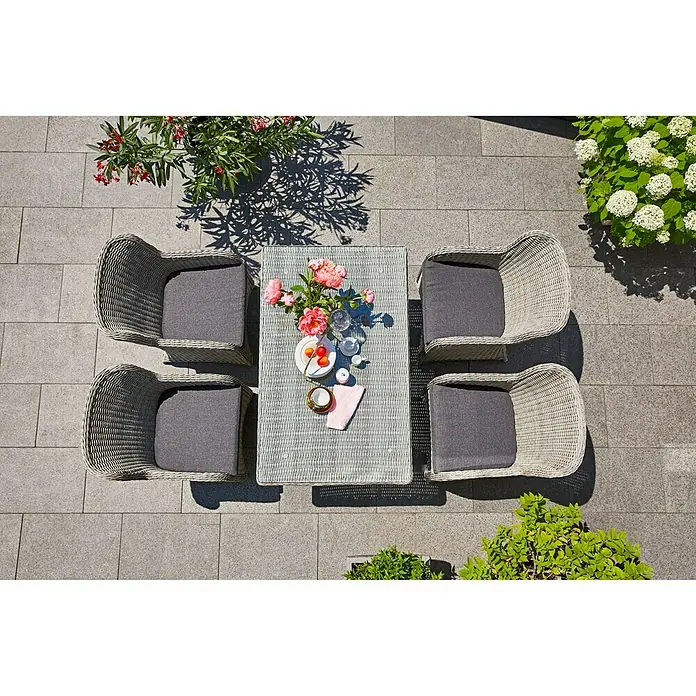 Sunfun Pauline Gartentisch - L x B x H: 130 x 80 x 68 cm, Polyrattan, Bambusgrau - Eine graue Gartengarnitur mit vier Korbstühlen und einem passenden Tisch, dekoriert mit Blumen und Geschirr, steht auf einer Terrasse.