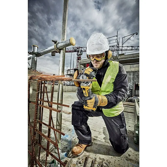 DeWalt XR 18V Amoladora angular de batería DCG405NT - 18 V, Sin batería, Diámetro disco: 125 mm, Número de revoluciones de marcha en vacío: 9.000 r.p.m. - Un trabajador de la construcción arrodillado cortando vigas de acero con una amoladora Dewalt, con medidas de seguridad.