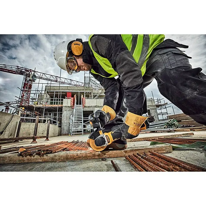 DeWalt XR 18V Amoladora angular de batería DCG405NT - 18 V, Sin batería, Diámetro disco: 125 mm, Número de revoluciones de marcha en vacío: 9.000 r.p.m. - Un trabajador de la construcción utiliza una amoladora angular DeWalt en una obra para cortar metal. Lleva equipo de protección.