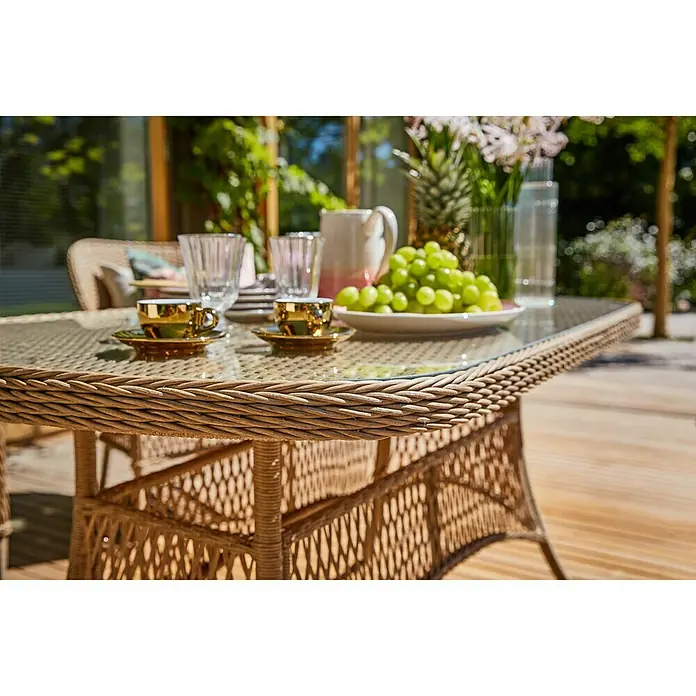 Sunfun Mesa de jardín Sophie - L x An x Al: 140 x 80 x 72 cm, Aluminio, Beige - Primer plano de una mesa de ratán con tapa de cristal, tazas doradas, vasos, una jarra, una piña y uvas, mostrando una elegante escena de jardín.