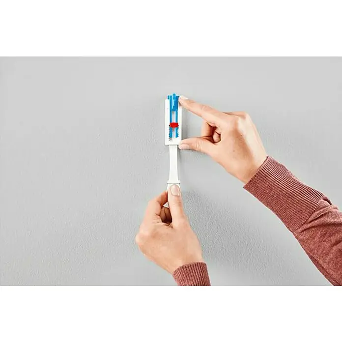 Tesa Clavo adhesivo Lienzo - Blanco, Carga soportada: 2 kg, 2 ud., Paredes pintadas - Una persona está montando un soporte de pared especial, hecho de plástico y con un sistema de nivelación integrado.