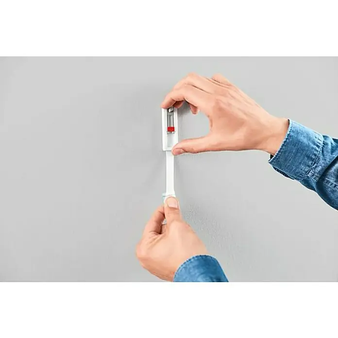 Tesa Clavo adhesivo - Carga soportada: 0,5 kg, 2 ud., Paredes pintadas, Blanco - Un anclaje de pared instalado a mano en una pared gris, lo que demuestra la instalación del producto o el montaje seguro.