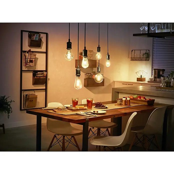 Philips Hue Bombilla LED inteligente Filamento blanco - E27, Intensidad regulable, Blanco cálido, 550 lm, 7 W, Denominación de la lámpara: ST64 - Una acogedora escena de comedor con una llamativa lámpara colgante con diferentes bombillas Edison, que proyecta un cálido resplandor.
