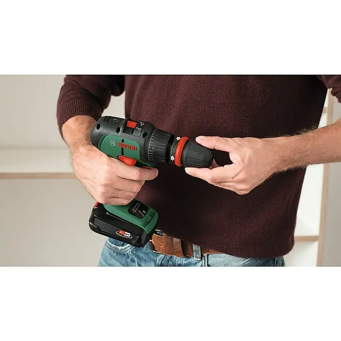 Bosch Power for All 18V Akku-Schlagbohrschrauber AdvancedImpact 18 - 18 V, 2 Akkus, 2,5 Ah - Nahaufnahme eines Mannes, der einen kabellosen Bosch-Bohrer hält und den Bohreraufsatz wechselt, im Hintergrund ein Regal.