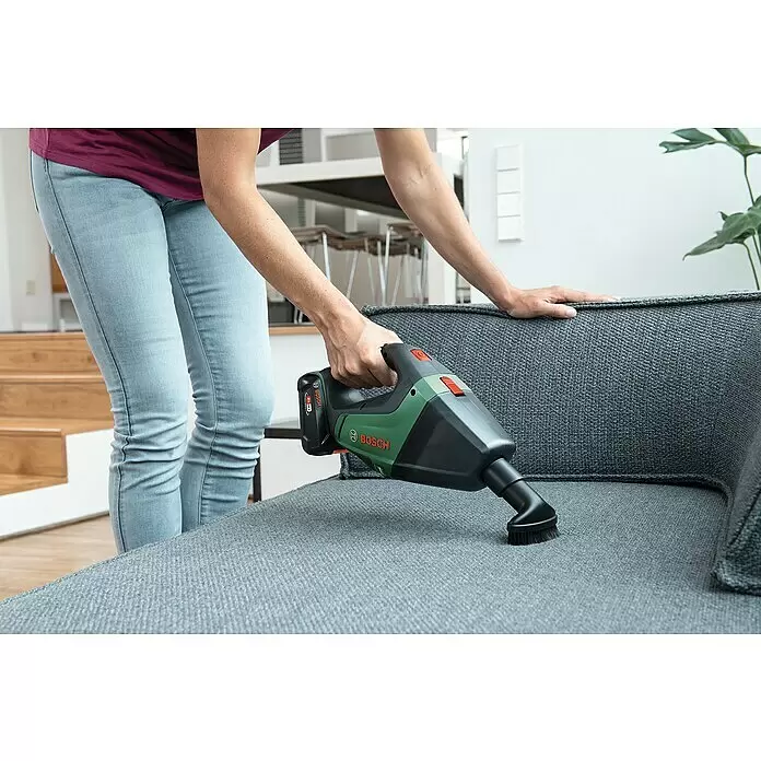 Bosch Power for All 18V Aspirador de mano de batería UniversalVac - 18 V, 1 batería, 2,5 Ah, Volumen de recipiente: 0,5 l - Aspiradora de mano Bosch verde y negra limpiando un sofá gris.