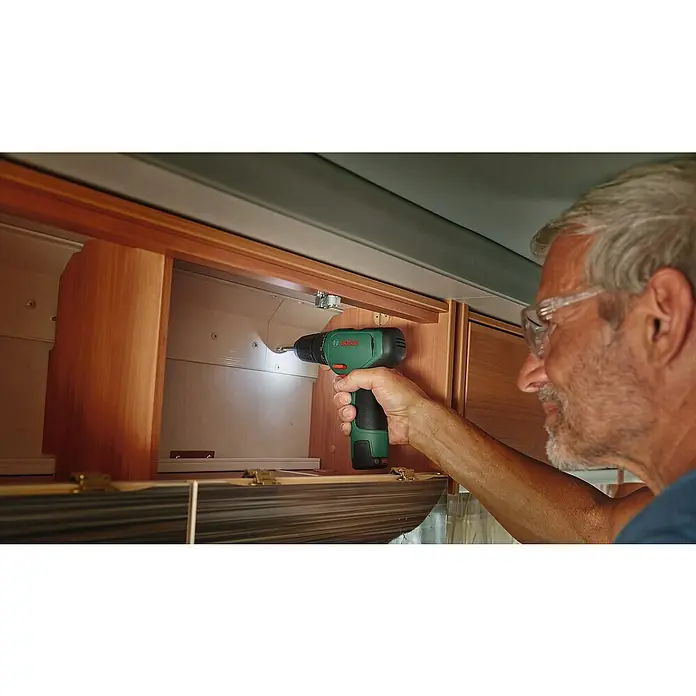 Bosch Power for All 12V Akku-Bohrschrauber EasyDrill 1200 - 12 V, 1 Akku, 1,5 Ah, 30 Nm - Ein Mann befestigt eine Holzstruktur mit einem grünen Bosch Akku-Bohrschrauber an einer weißen Wand. Das Werkzeug ist der Fokus des Bildes.