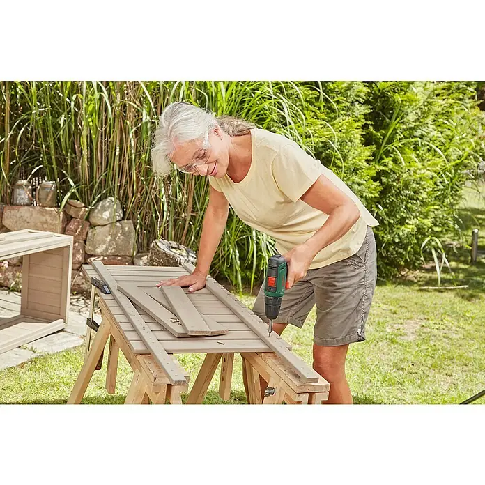 Bosch Power for All 12V Akku-Bohrschrauber EasyDrill 1200 - 12 V, 2 Akkus, 1,5 Ah - Eine ältere Frau benutzt einen Akkuschrauber, um im Freien ein Holzprojekt zu bearbeiten. Sie trägt dabei eine Schutzbrille.