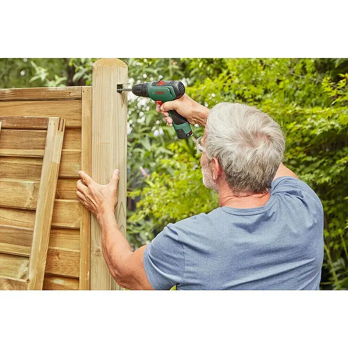 Bosch Power for All 12V Akku-Bohrschrauber EasyDrill 1200 - 12 V, 2 Akkus, 1,5 Ah - Ein Mann arbeitet mit einem grünen Bosch-Akkuschrauber an einem Holzzaun im Garten. Der Akkuschrauber ist ideal für Heimwerkerprojekte.