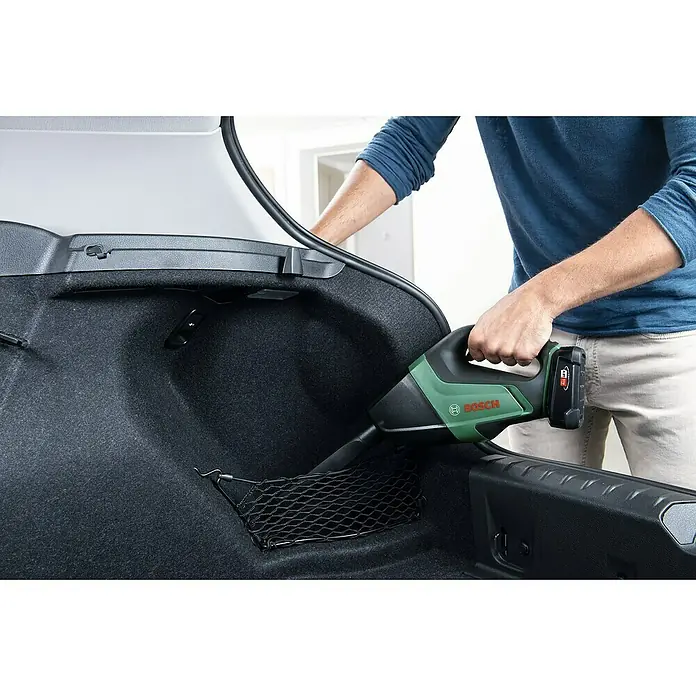 Bosch Power for All 18V Akku-Handstaubsauger UniversalVac 18 - 18 V, Ohne Akku, Behältervolumen: 0,5 l - Eine Person saugt mit einem Bosch-Akkusauger den Kofferraum eines Autos. Das Gerät ist grün-schwarz und mit einem Akku ausgestattet.