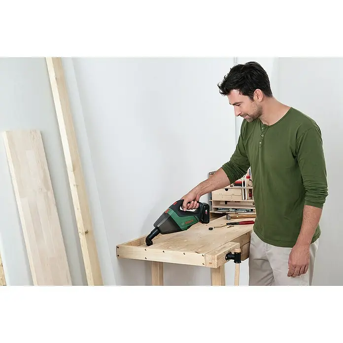 Bosch Power for All 18V Akku-Handstaubsauger UniversalVac 18 - 18 V, Ohne Akku, Behältervolumen: 0,5 l - Ein Mann benutzt einen Bosch Akku-Handsauger, um eine Werkbank von Holzstaub zu befreien. Das Gerät ist kompakt und ideal für kleine Reinigungsarbeiten.