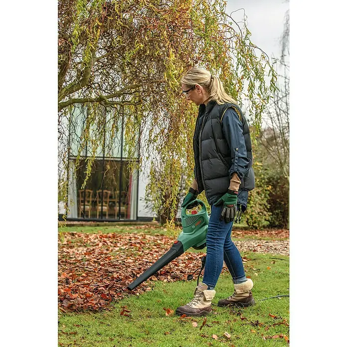 Bosch Elektro-Laubsauger UniversalGardenTidy 3000 - 3.000 W, Blasgeschwindigkeit: 165 km/h - 285 km/h - Frau benutzt einen Laubbläser von Bosch im Garten, um die Blätter zu entfernen.