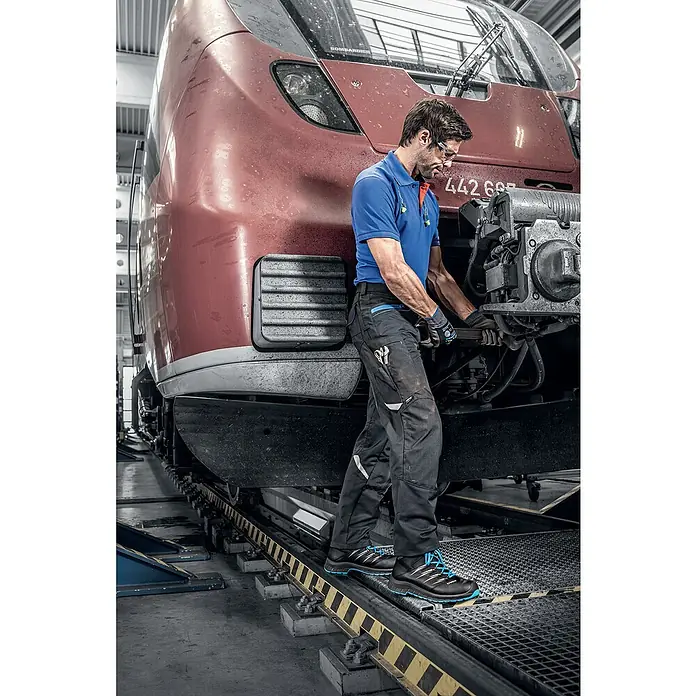 Uvex 2 Trend Sicherheitsstiefel S3 - 47, Schutzklasse nach EN ISO 20345: S3, Schwarz/Blau - Ein Mann in Arbeitskleidung mit Uvex-Sicherheitsschuhen bei der Arbeit an einer Lokomotive.