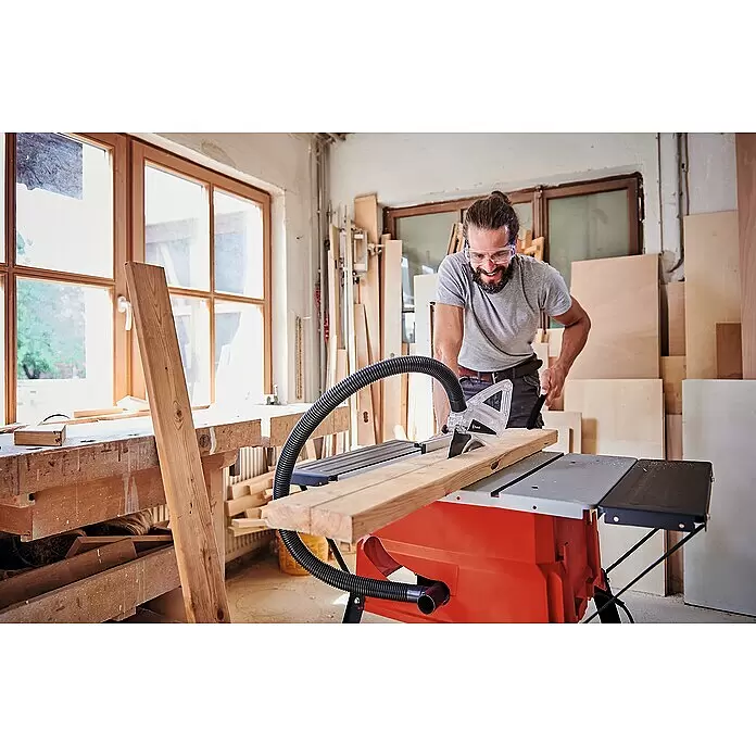 Einhell Sierra circular de mesa TC-TS 2025/2 U - 1.800 W, Diámetro hoja de sierra: 250 mm, Profundidad de corte a 90 °: 85 mm - Hombre con gafas de seguridad cortando madera en una sierra de mesa naranja y gris en un taller.