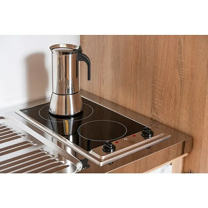 Respekta Schrankküche Peter - Breite: 104 cm, Weiß/Eiche, Mit Glaskeramikkochfeld und Mikrowelle - Eine elegante Moka-Kanne aus Edelstahl steht auf einem modernen Kochfeld mit zwei Kochplatten und Bedienknöpfen.