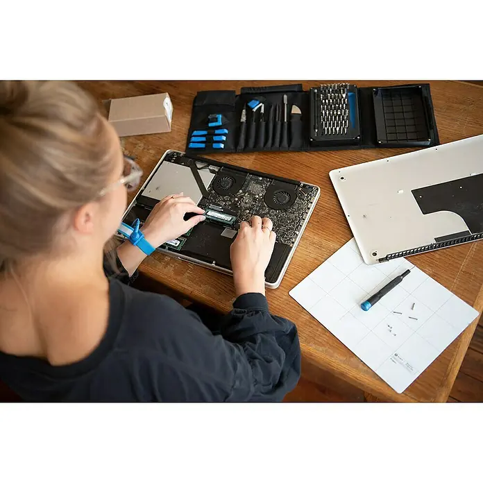 iFixit Set de herramientas Pro Tech - 84 pzs. - Una persona trabajando en un portátil abierto, con un kit de herramientas y una alfombrilla para tornillos al lado.