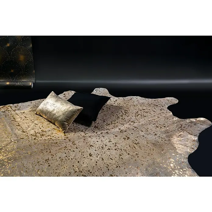 Esbeco Kuhfell Gefleckt - Gold, 100 % Echtfell - Goldener Teppich mit Kissen und einer Rolle Tapete im Hintergrund.