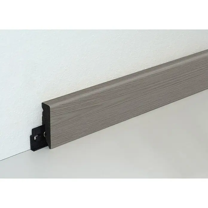 Profiles and more Sockelleiste KU051L Woodstock Eiche - Woodstock Eiche, 240 cm x 15 mm x 50 mm - Ein Detailaufnahme einer modernen, grauen Fußleiste mit Clip-System, die zwischen Wand und Boden angebracht ist. Sie hat eine feine Holzmaserung.