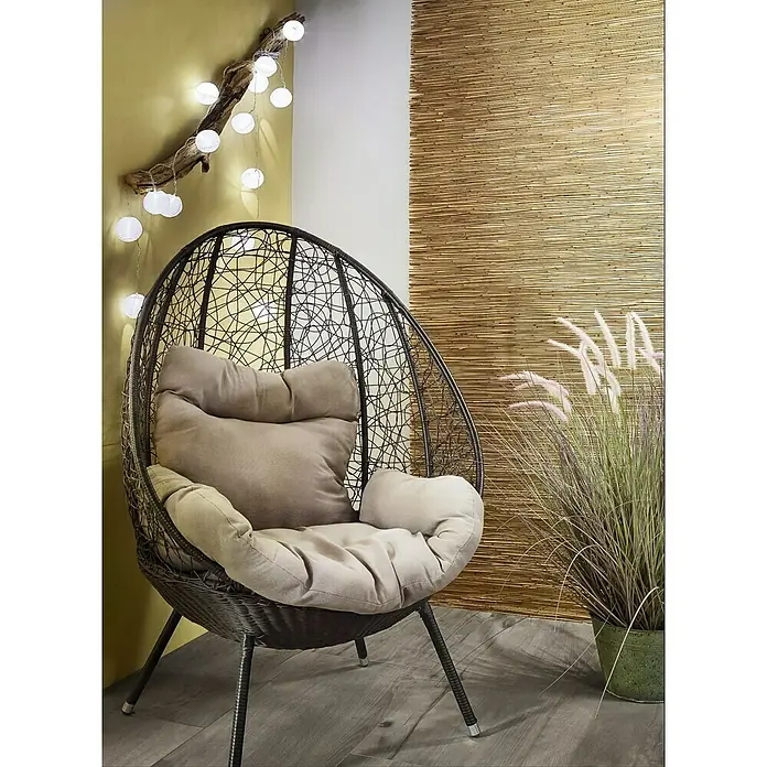 Paulmann Guirnalda luminosa LED Lampion - 3,6 m, Para exterior - Cómoda silla colgante de ratán con cojines beige frente a una pared de bambú e hilo de luces, perfecta para relajarse en el hogar.