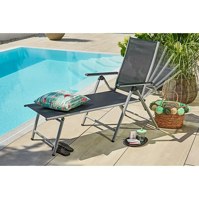Sunfun Marina Gartenliege - Schwarz/Silber, Aluminium, Rückenlehne verstellbar - Ein grauer Liegestuhl mit verstellbarer Rückenlehne, auf dem eine Kissen liegt, steht am Pool. Daneben ein Korb und ein kleines Tablett mit Getränk.