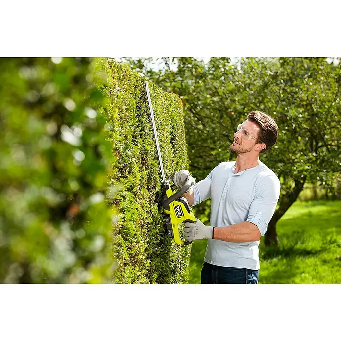 Ryobi ONE+ Akku-Heckenschere OHT1845 - 18 V, Li-Ionen, Ohne Akku, Schnittlänge: 45 cm - Ein Mann benutzt eine RYOBI Heckenschere, um eine Hecke zu schneiden, wobei er eine Schutzbrille und Handschuhe trägt.