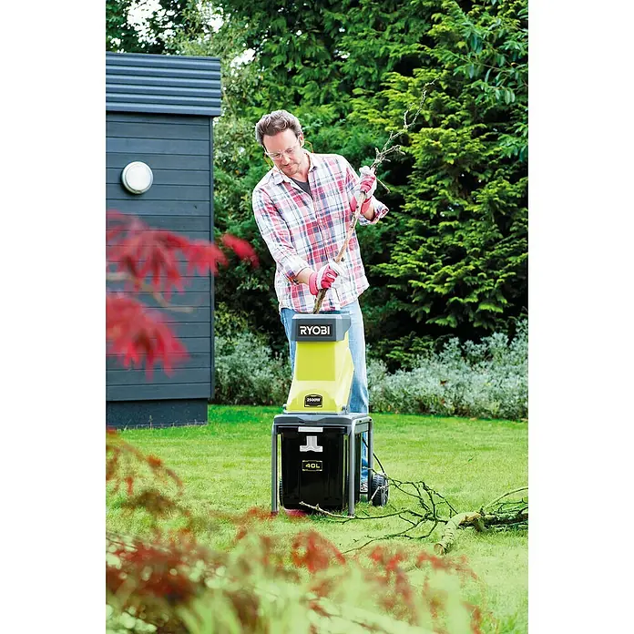 Ryobi Elektro-Häcksler RSH2545B - Max. Aststärke: 4,5 cm, 2.500 W - Mann bedient einen RYOBI 2500W Häcksler im Garten, um Äste zu zerkleinern. Der Behälter des Häckslers fasst 40 Liter.