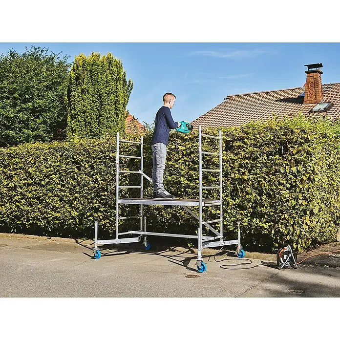 Krause ClimTec Rollgerüst - Arbeitshöhe: 3 m - Ein Mann steht auf einem Gerüst und schneidet eine Hecke mit einer Heckenschere. Das Gerüst verfügt über Rollen für mehr Flexibilität.