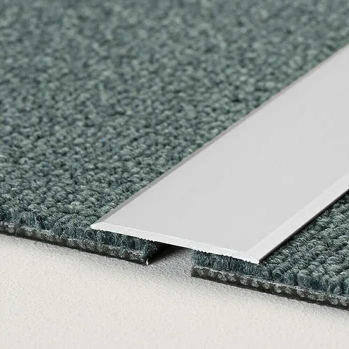LOGOCLIC Übergangsprofil 115 - Silber, 1 m x 40 mm x 2 mm, Montageart: Kleben - Das Bild zeigt eine Übergangsschiene aus Metall, die zwischen zwei Teppichböden unterschiedlicher Höhe platziert ist, um einen nahtlosen Übergang zu schaffen.
