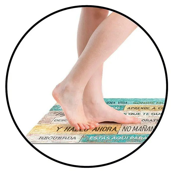 Alfombra de vinilo Croma Etnic stone - Blanco/Marrón/Negro, 75 x 45 cm - Un primer plano de una alfombra de baño con citas inspiradoras en español y pies sobre ella.