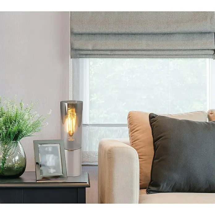 Globo Annika Lámpara de sobremesa - 25 W, Ø x Al: 9 x 30 cm, Níquel, E27 - Una lámpara de mesa decorativa con una pantalla transparente y una bombilla Edison emite una luz cálida, ubicada en un espacio habitable elegante.