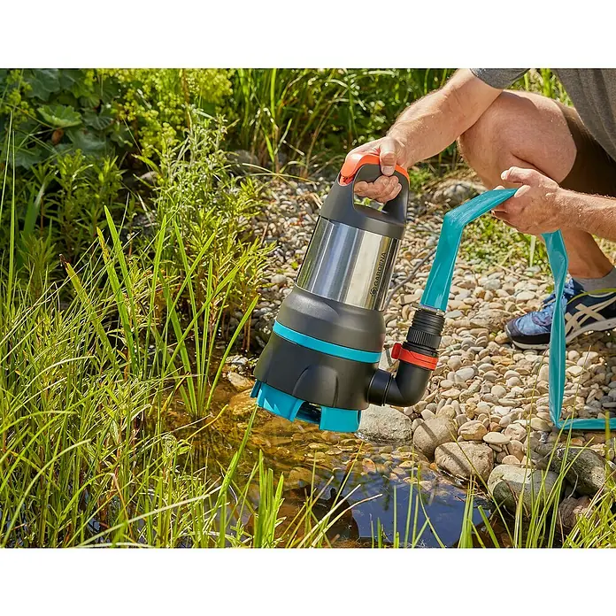 Gardena Schmutzwasserpumpe 19500 Aquasensor - 860 W, Max. Fördermenge: 19.500 l/h - Eine GARDENA Schmutzwasser-Tauchpumpe wird in einen Teich gehalten, um das Wasser abzupumpen. Der blaue Schlauch ist angeschlossen.