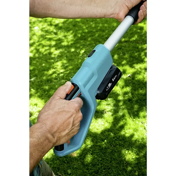 Gardena Power for All 18V Teleskop-Heckenschere - 18 V, 1 Akku, Schwertlänge: 42 cm - Nahaufnahme einer Gardena Akku-Grasschere mit Teleskopstiel in Aktion, gehalten von einer Person vor einem grünen Rasen.