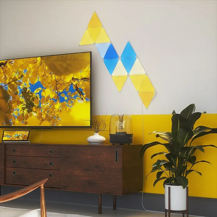 Nanoleaf Starterkit Shapes Triangles 15 Panels - 15 Stk., Weiß, RGBW, Triangles, Smart Home-fähig: Ja - Buntes Nanoleaf Lines-Wandpaneel-Design, das über einem Sideboard mit TV und Zimmerpflanze in einem modernen Wohnzimmer hängt.