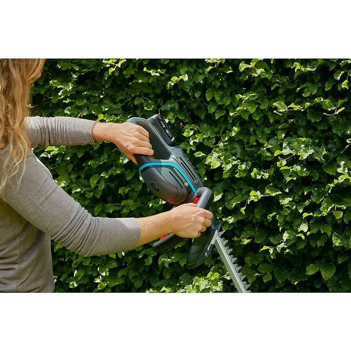 Gardena Power for All 18V Akku-Heckenschere ComfortCut 50 - 18 V, Li-Ionen, Ohne Akku, Schwertlänge: 50 cm - Nahaufnahme einer Person, die eine Gardena Akku-Heckenschere vor einer grünen Hecke bedient.