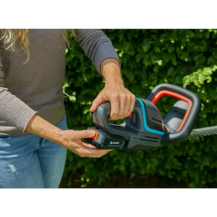 Gardena Power for All 18V Akku-Heckenschere ComfortCut 50 - 18 V, Li-Ionen, 1 Akku, Schwertlänge: 50 cm - Eine Person hält eine Gardena Akku-Heckenschere in der Hand. Das Gerät ist schwarz mit orangen und blauen Akzenten.