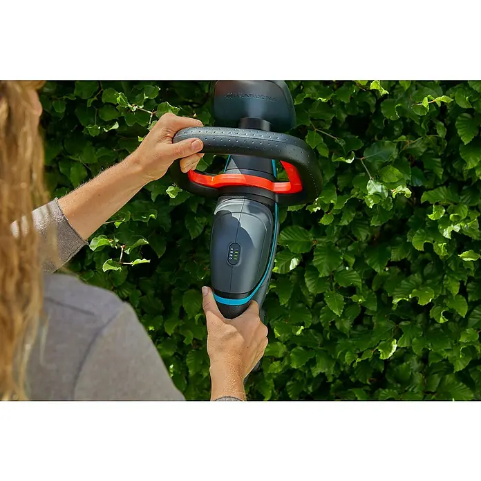 Gardena Power for All 18V Akku-Heckenschere ComfortCut 50 - 18 V, Li-Ionen, 1 Akku, Schwertlänge: 50 cm - Eine Person benutzt eine Gardena Akku-Strauchschere vor einer grünen Hecke. Die Bedienelemente und das Design der Schere sind gut sichtbar.