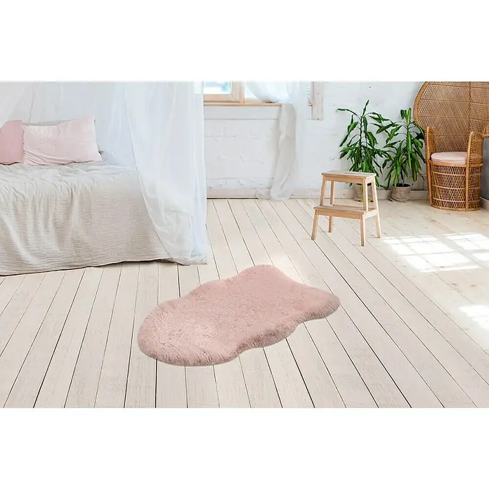 Kunstfell Happy - Rosa, 90 x 60 cm, 100 % Polyester (Flor) - Rosa Schaffellteppich auf hellem Holzboden in einem hellen Raum mit Bett und Pflanzen. Ein weicher Akzent für jedes Zimmer.