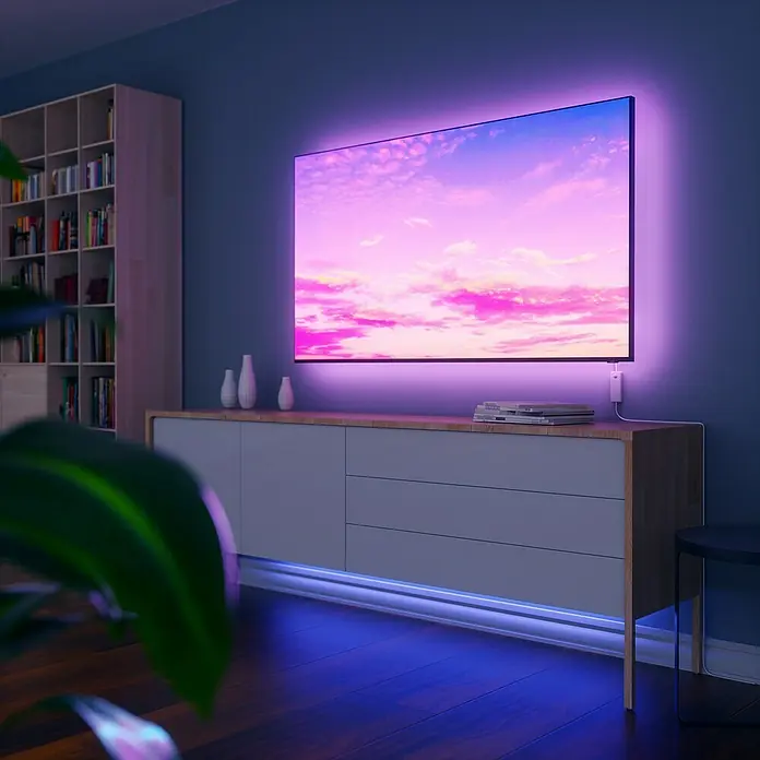 Nanoleaf Smart-LED-Band Essentials Lightstrip Erweiterungskit - 23 W, Weiß, Länge: 1 m, RGBW - Das Bild zeigt ein modernes Wohnzimmer mit einem Smart-TV mit LED-Hintergrundbeleuchtung und indirekter Beleuchtung unter einem Sideboard.
