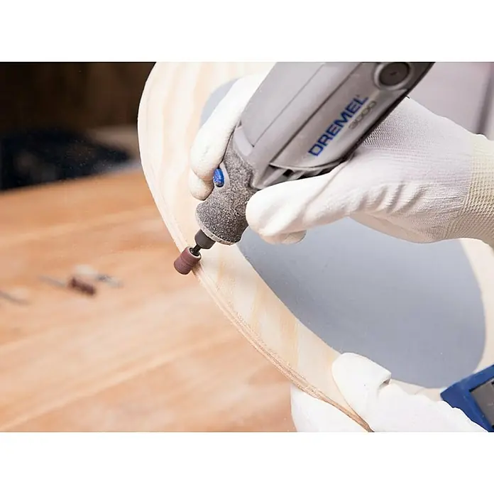 Dremel Multifunktionswerkzeug-Zubehör 681 - 20 -tlg. - Nahaufnahme eines Dremel 3000 beim Schleifen eines Holzstücks. Die Hände tragen weiße Handschuhe für Schutz bei der Holzarbeitung.