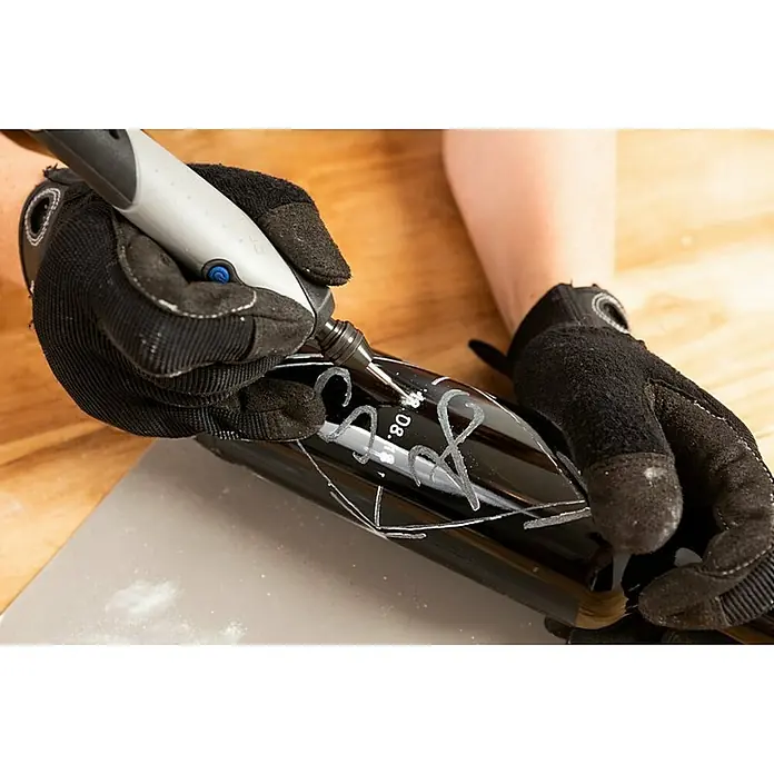 Dremel Glasbearbeitungs-Set 682 - 8 -tlg., Durchmesser Schaft: 3,2 mm - Eine Person graviert mit einem Dremel-Werkzeug ein schwarzes Objekt, wobei sie Handschuhe trägt. Das gravierte Muster ist erkennbar.