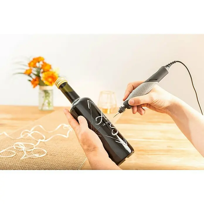Dremel Glasbearbeitungs-Set 682 - 8 -tlg., Durchmesser Schaft: 3,2 mm - Nahaufnahme einer Person, die mit einem Dremel-Gravierwerkzeug ein personalisiertes Design auf eine Glasflasche graviert.