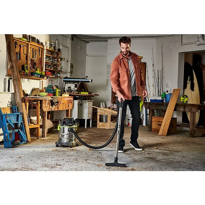 Ryobi ONE+ Akku-Nass-Trockensauger R18WDV-0 - 18 V, Ohne Akku, Behältervolumen: 18 l - Ein Mann benutzt einen RYOBI Akku-Nass-Trockensauger, um eine Werkstatt zu reinigen. Der Sauger ist aus Edelstahl und hat einen schwarzen Schlauch.