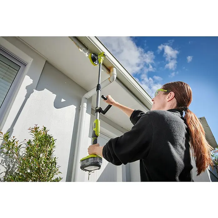 Ryobi ONE+ Akku-Reinigungsbürste R18TPS-0 - 18 V, Ohne Akku - Eine Frau benutzt einen Ryobi-Gerätereiniger mit Bürste, um eine Dachrinne von Blättern und Schmutz zu befreien. Das Gerät ist kabellos und akkubetrieben.