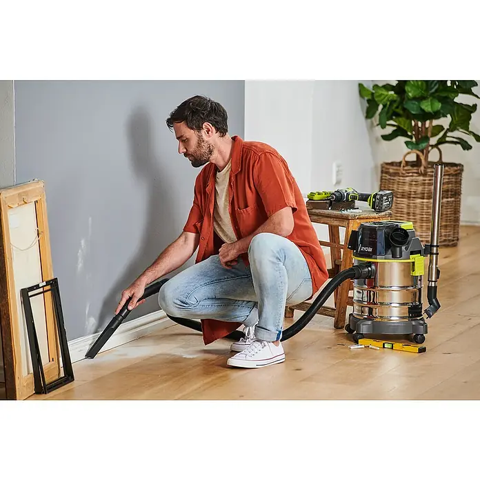 Ryobi ONE+ Akku-Nass-Trockensauger R18WDV-0 - 18 V, Ohne Akku, Behältervolumen: 18 l - Mann saugt mit einem Ryobi Akku-Nass-/Trockensauger Schmutz an einer Wand auf. Das Gerät verfügt über einen robusten Tank und hohe Mobilität für vielfältige Reinigungsarbeiten.